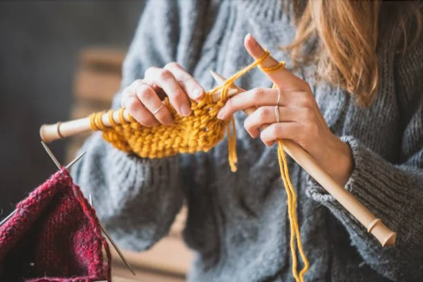 Woman knitting a yellow scarf in a cozy home setting