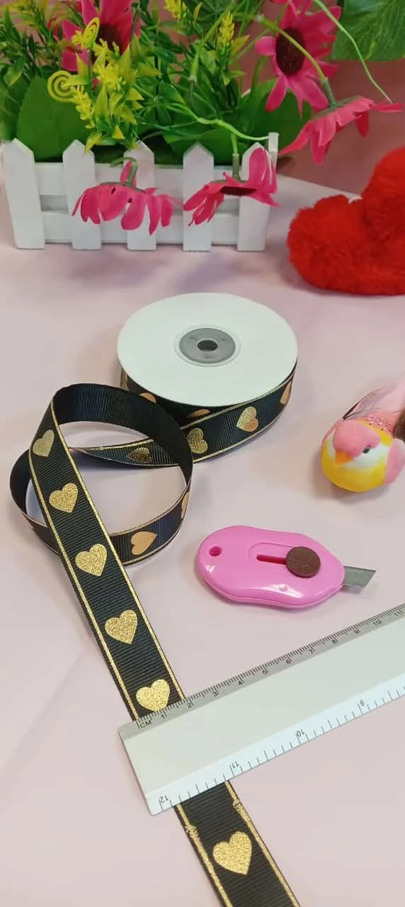 Black ribbon with gold hearts, ruler, and pink cutter for crafting