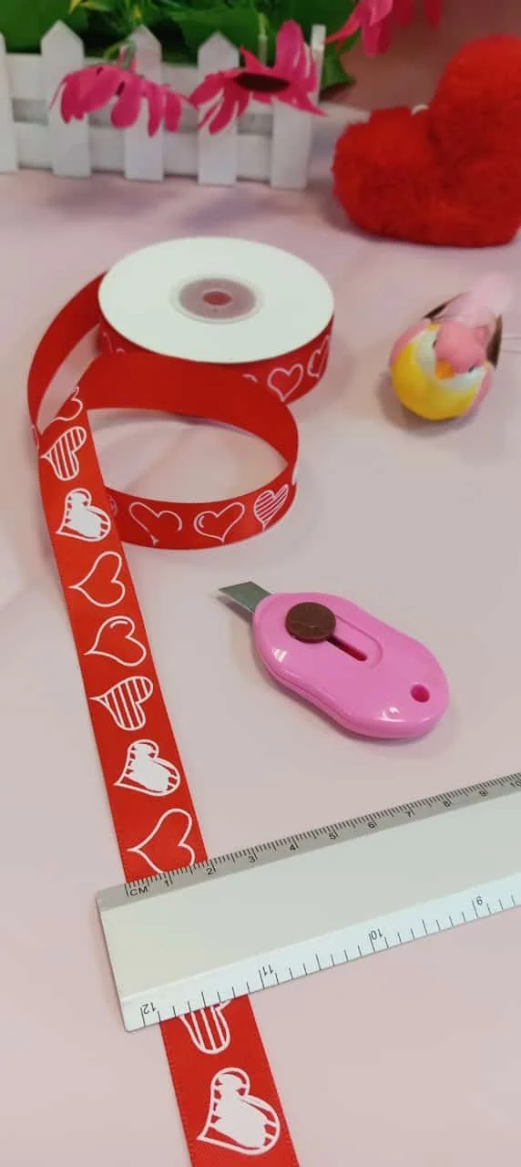 Red ribbon with hearts, ruler, and craft knife, part of "Listones Love" craft supplies.
