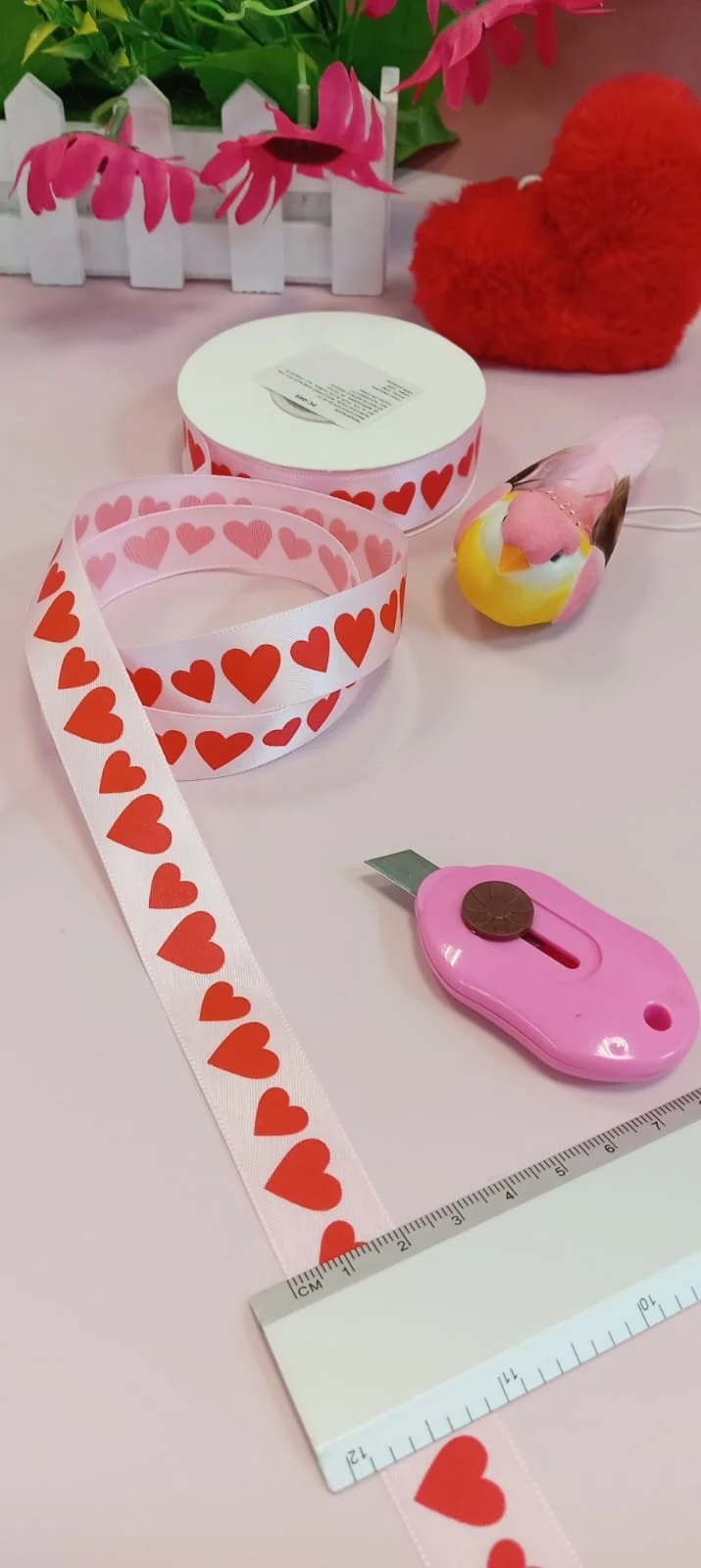 Pink ribbon with red hearts, ruler, and cutter for crafting