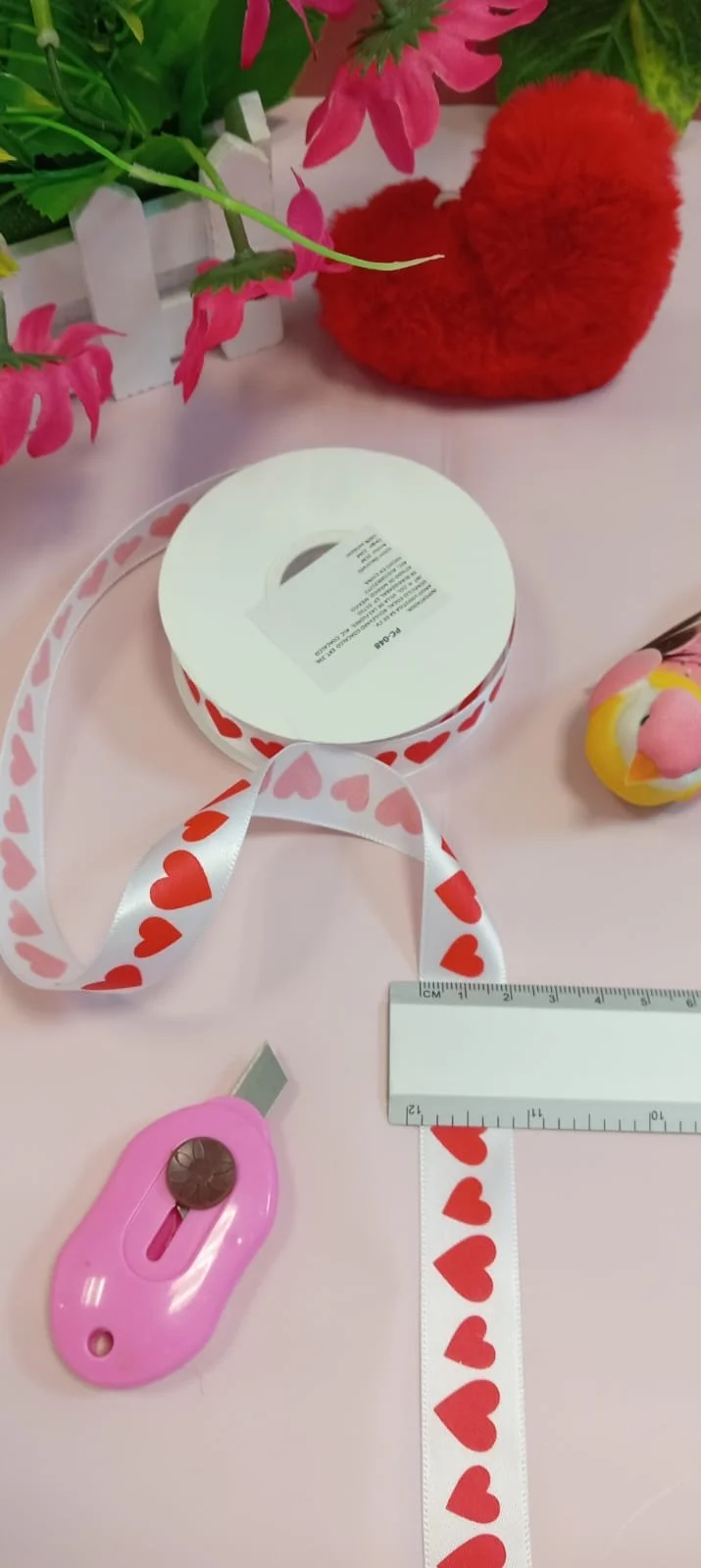 White ribbon with red hearts, pink craft knife, and ruler for crafting.